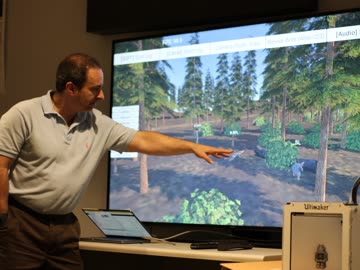Researcher pointing at a virtual forest scene on a wall display